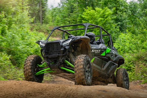 Three-quarter front angle of a driver and passengers in a side x side scaling a small hill on a wooded trail. opens in a new window