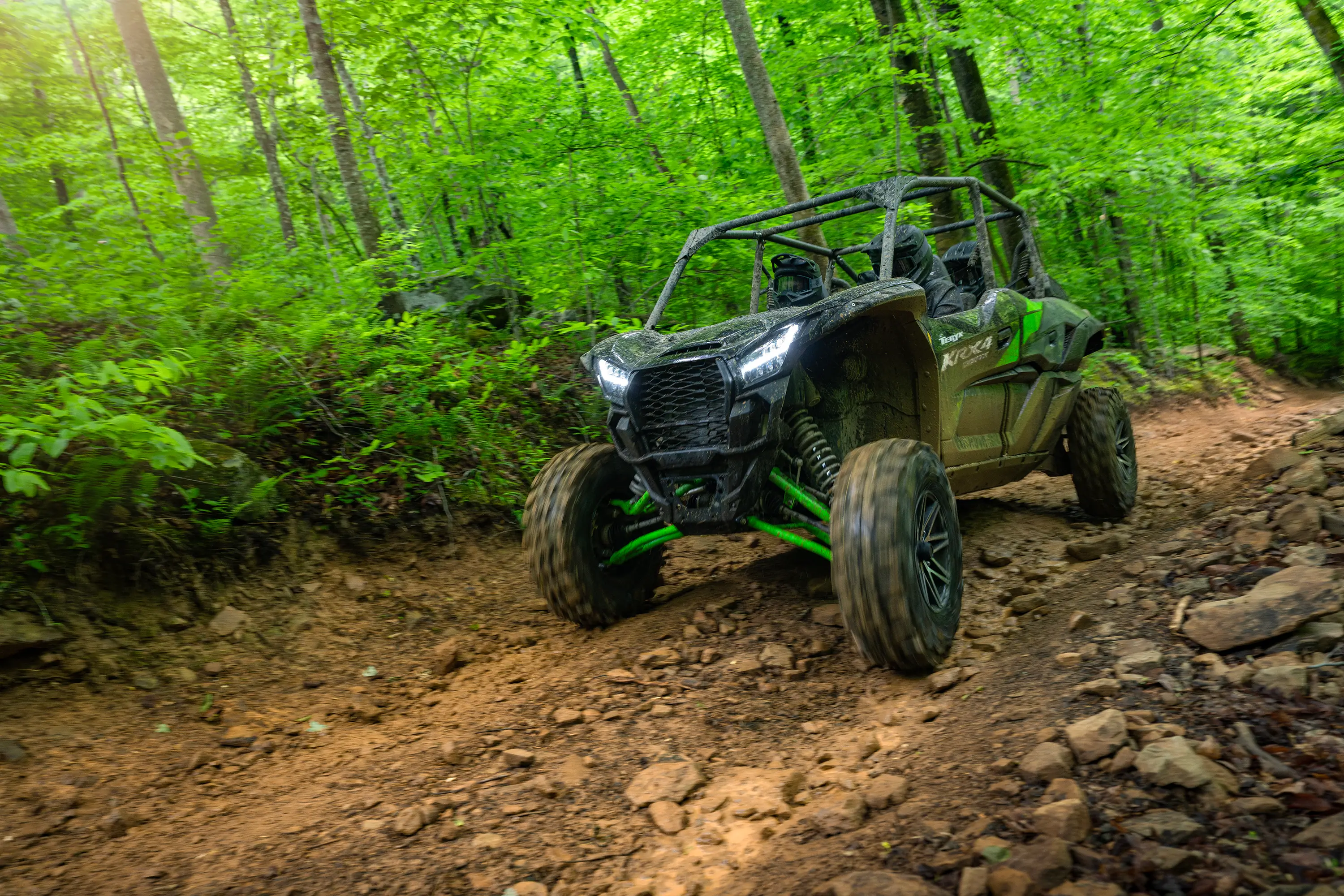 Three-quarter front angle of a driver and passengers in a side x side riding on a forest trail.