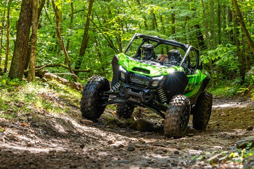 Three-quarter front angle of a person driving a side x side through mud. opens in a new window